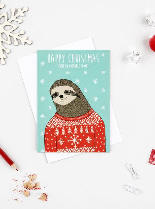 sloth christmas card featuring a sloth wearing a red christmas sweater with a blue background and snowflakes falling. Text above the sloth says 'Happy Christmas from an adorable sloth' Illustrative style.