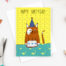 Photograph of a card featuring a ginger cat having a brthday party wearing a party hat and in front of a cake! Yellow spotty background with the wording 'Happy birthday' above
