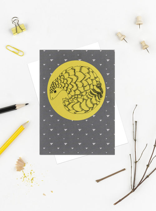 Greetings card featuring a yellow circle with an illustration of a pangolin. Black ink illustration of a pangolin curled up.