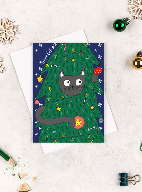 Chrstmas card featuring a black cat hidden in a christmas tree playing with baubles